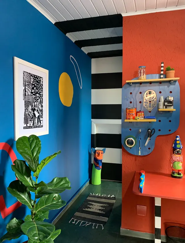 Ateliê com parede azul e vermelha, listras pretas e brancas e pegboard azul com ferramentas