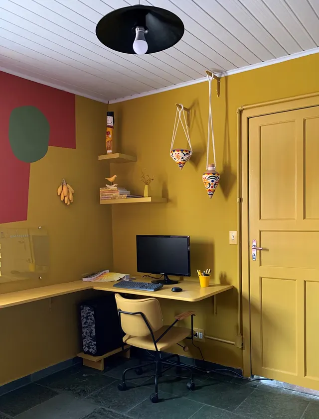 Home office com paredes amarelo ocre, bancada sob medida e porta pintada na mesma cor