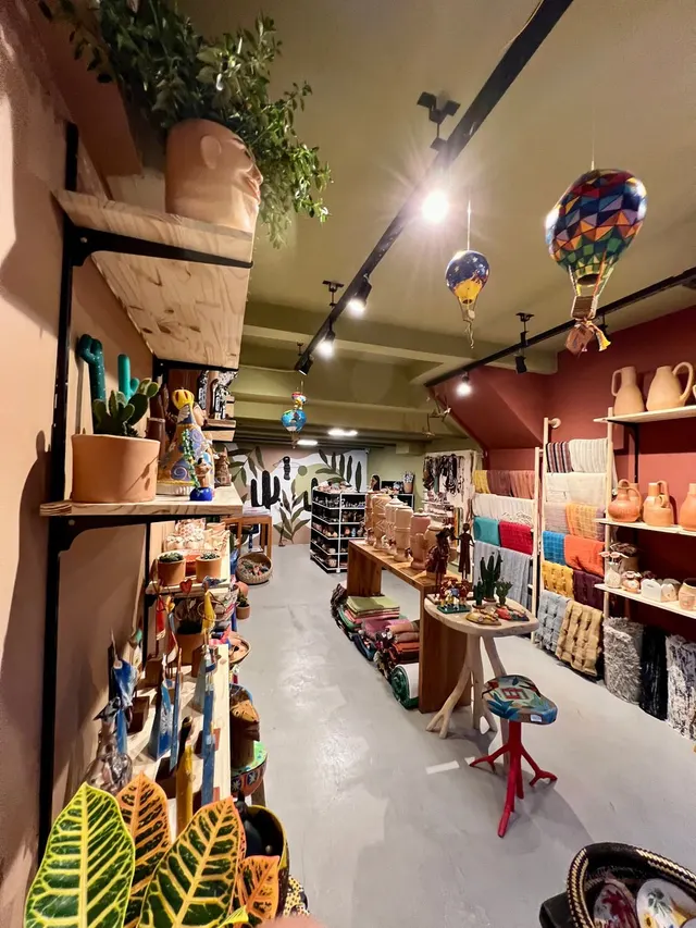 Loja de artesanato com prateleiras de madeira, cerâmica popular, tecidos coloridos e balões de papel pendurados no teto