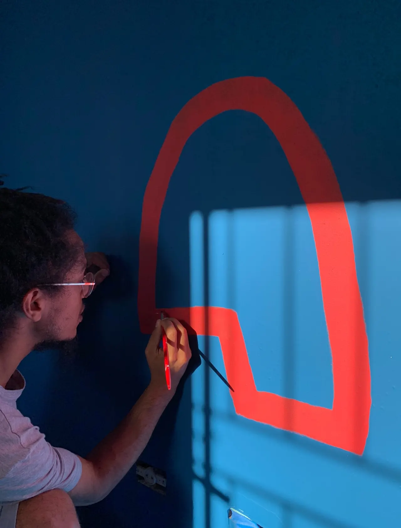 Jorge pintando à mão um arco vermelho sobre parede azul no ateliê da Orí