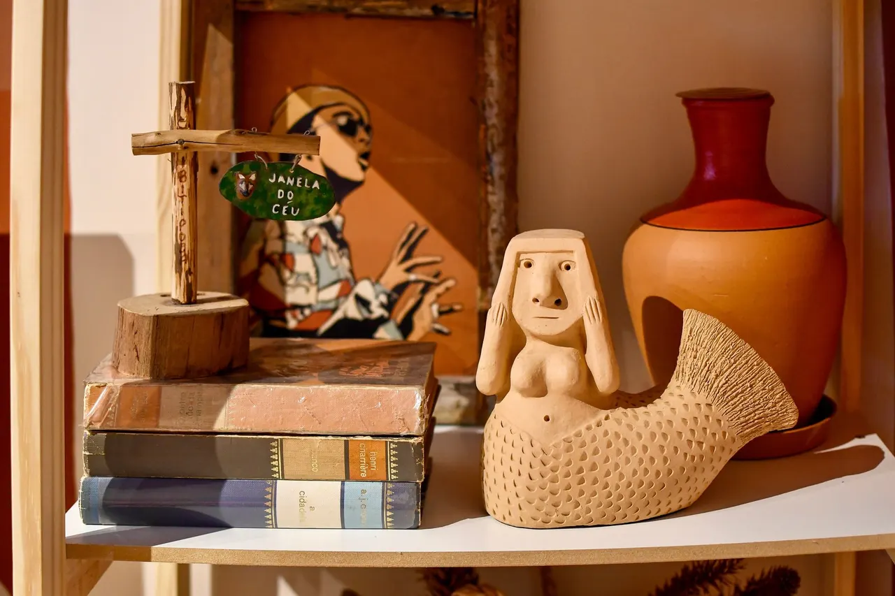 Prateleira com cerâmica popular brasileira, livros antigos e uma escultura de sereia em barro