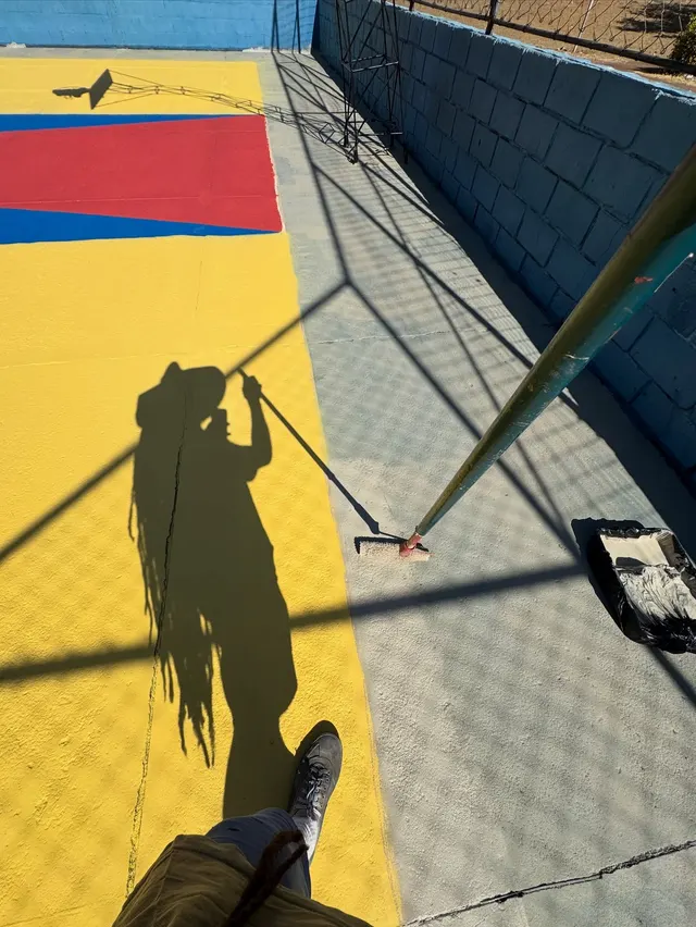 Sombra do Jorge pintando com rolo o piso amarelo e vermelho de uma quadra