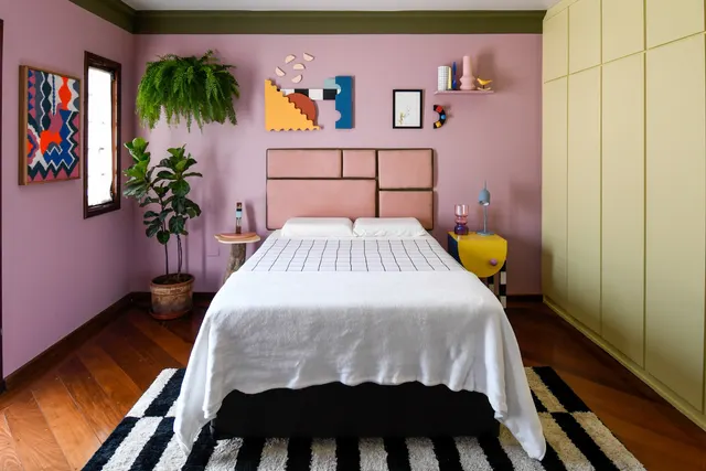O quarto depois: parede rosa, cabeceira geométrica estofada, peças de arte na parede e tapete listrado