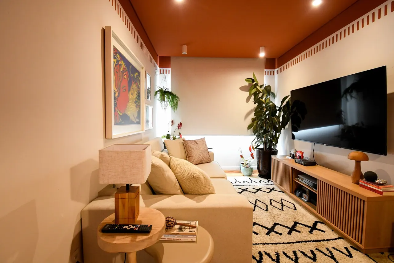 Sala com teto pintado em terracota, sofá claro, quadro colorido e tapete de padrão preto e branco