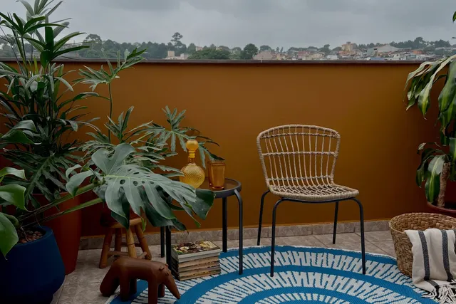 A varanda depois: muro ocre, cadeira de fibra, tapete azul redondo e plantas grandes